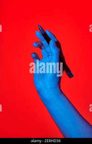 La mano blu della donna su sfondo rosso, scrivendo con una penna. Foto verticale isolata Foto Stock