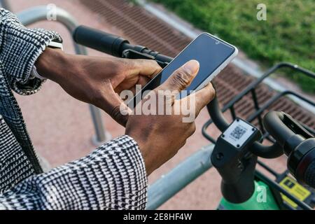 Dall'alto di raccolto anonimo etnia lavoratore di ufficio maschile utilizzando applicazione su cellulare con schermo nero mentre si parcheggia la bicicletta città Foto Stock