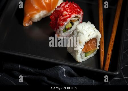 Vista dall'alto composizione di deliziosi sushi e bambù freschi i bastoncini serviti su un piatto nero su un panno a scacchi Foto Stock