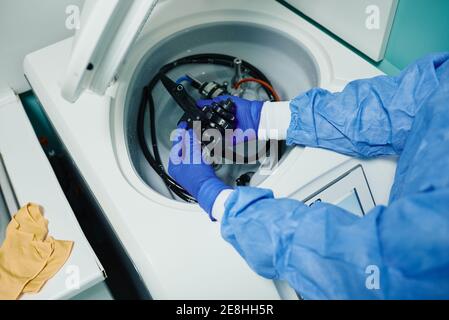 Dall'alto del prodotto medico irriconoscibile in guanti sterili e. camicetta che mette l'endoscopio nella centrifuga della macchina di disinfezione dopo la procedura Foto Stock