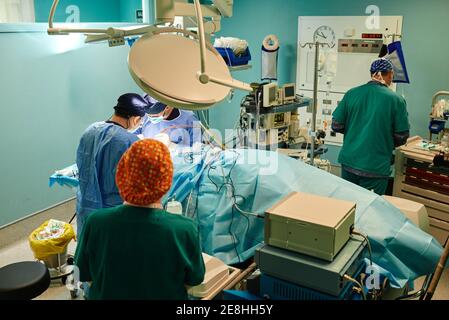 Vista dall'alto del retro di un assistente medico non riconoscibile che lascia il lavoro camera mentre un gruppo di medici che eseguono interventi chirurgici in clinica moderna Foto Stock