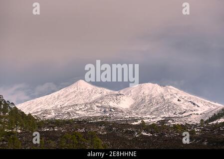 Pittoresco scenario di catena montuosa rocciosa con pendii coperti spesso strato di neve situato su vasta valle ruvida sotto cielo blu Foto Stock