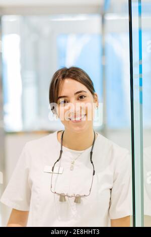 Sorridente attraente dottore femminile in bianco accappatoio in piedi in contemporanea clinica leggera e guardando la macchina fotografica felicemente Foto Stock