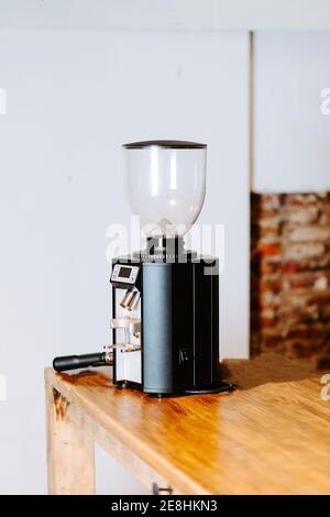 Macinacaffè in stile contemporaneo collocato sul banco in legno della caffetteria con interni luminosi Foto Stock