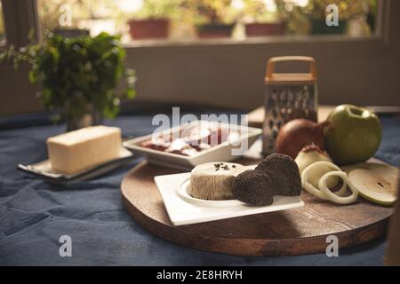 Tartufi su piatto vicino a formaggi e cipolle crude con mela sul tagliere in casa Foto Stock