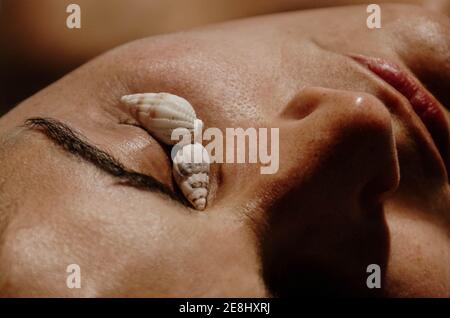 Closeup di raccolto anonimo giovane turista femminile che copre gli occhi con conchiglie mentre si prende il sole sulla spiaggia alla luce del sole Foto Stock