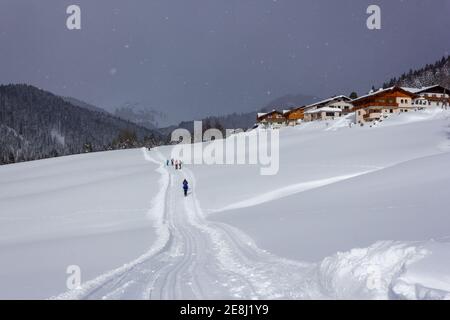 Diversi turisti escursioni durante il tempo nevoso nelle Alpi con Tipiche case austriache sullo sfondo Foto Stock