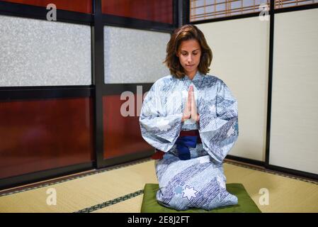 Ritratto interno di giovane in ginocchio attraente donna caucasica con le mani in preghiera indossando un tradizionale kimono giapponese all'interno di una casa, Ainokura, Ja Foto Stock