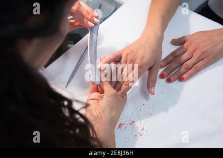 Angolo alto di raccolto anonimo maestro di bellezza chiodo di archiviazione di Donna utilizzando il bordo di smeriglio durante la procedura di manicure a tavola Foto Stock