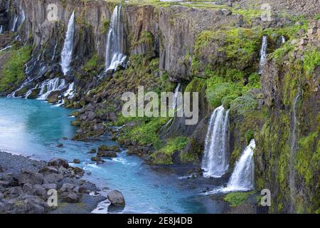Spettacolare vista delle rapide cascate che scorrono dalla ruvida scogliera rocciosa coperto di verde lussureggiante in una tranquilla riserva blu in pace natura Foto Stock
