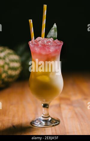 Bicchiere di fresco cocktail Pina Colada dolce guarnito con verde foglie e serviti su tavolo di legno in camera buia Foto Stock