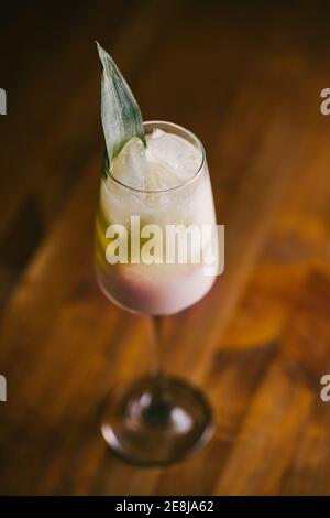 Da sopra un bicchiere di fresco cocktail Pina Colada dolce guarnito con foglie verdi e servite su tavolo di legno Foto Stock