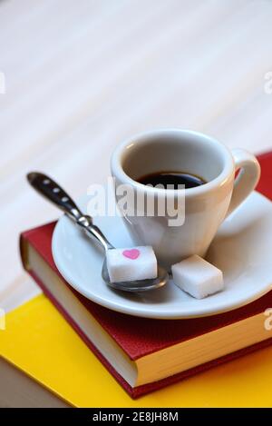 Tazza di caffè su libri e cucchiaio di caffè con cubetti di zucchero, espresso Foto Stock