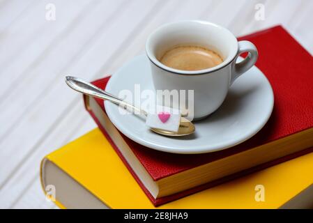 Tazza di caffè su libri e cucchiaio di caffè con cubetti di zucchero, espresso Foto Stock