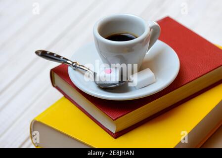 Tazza di caffè su libri e cucchiaio di caffè con cubetti di zucchero, espresso Foto Stock