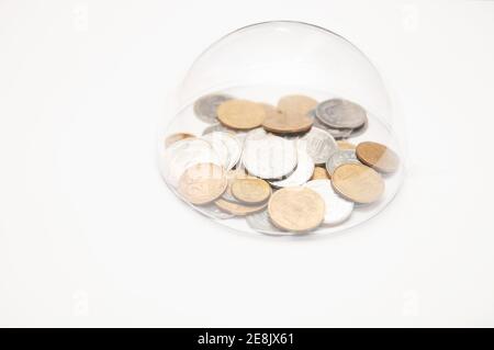 le monete metalliche sono raggruppate sotto un semicerchio di vetro su a. sfondo bianco Foto Stock