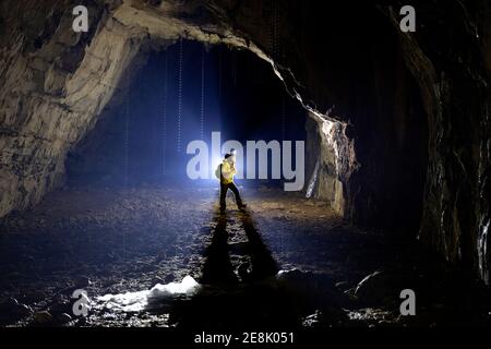 Ragazzo di 11 anni in piedi all'interno di una grotta, illuminato da una retroilluminazione, stalagmiti fuse di ghiaccio nella parte anteriore, Slovenia Foto Stock