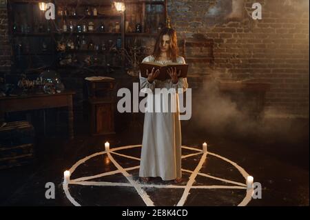 Donna con libro di incantesimi in piedi in cerchio magico Foto Stock