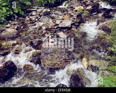 Primo piano del flusso rapido e pulito che scorre sulle rocce. Il fiume di montagna scorre giù e spruzzi Foto Stock