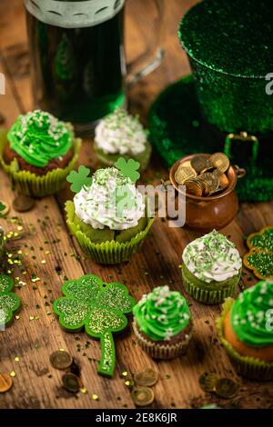 Cupcake decorati e pentola con monete d'oro su tavolo di legno. Festa di San Patrizio Foto Stock