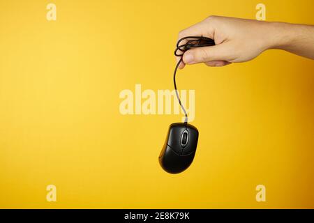 Il mouse nero a portata di mano su sfondo giallo con spazio di copia. Concetto di servizio di manutenzione hardware Foto Stock