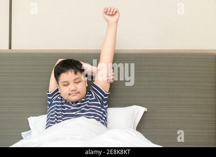 Il ragazzo grasso obeso si sveglia e si allunga sul letto al mattino, la sanità e il concetto del mondo del buon mattino Foto Stock