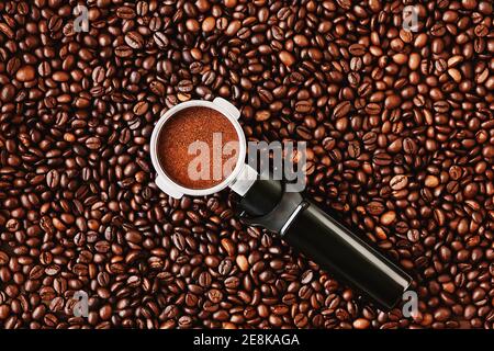 Il portafiltro della macchina da caffè, riempito con caffè macinato, si trova su uno sfondo di chicchi di caffè aromatici tostati. Preparare un caffè. Foto Stock