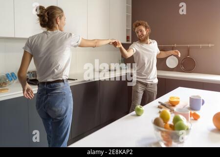 Waltzing in una nuova casa giovane coppia danzare celebrare il loro nuovo acquisto di acquistare la propria casa. Felice nuova famiglia in cucina da indossare casual Foto Stock