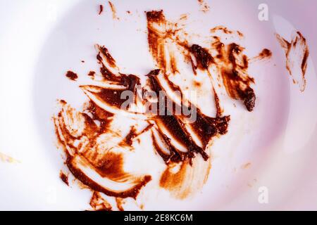 Vista ravvicinata della macchia di salsa di cioccolato mangiata con un piatto bianco sporco. Torta al cioccolato finita. Concetto di mangiare Foto Stock