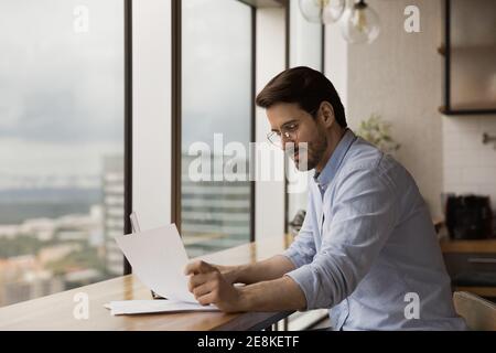 Un uomo d'affari che ha avuto successo a leggere il documento al banco di lavoro vicino alla finestra panoramica Foto Stock