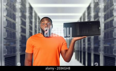 Sorpreso nero uomo tiene un server in mano. Concetto di hosting e storage Foto Stock