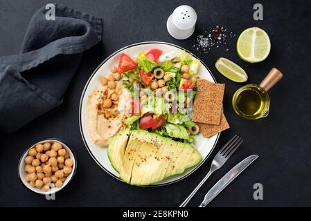 Insalata vegetariana vegana sana con avocado e hummus, pomodori, verdi e chikcpisei. Vista dall'alto Foto Stock