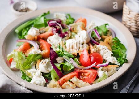 Insalata estiva italiana con mozzarella, insalata di foglie verdi, crostini, pomodori e capperi in un recipiente. Insalata vegetariana sana Foto Stock