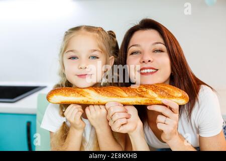 Famiglia felice, mamma e figlia mangiano un pane mordente da lati diversi. Rapporti familiari del bambino con i genitori Foto Stock