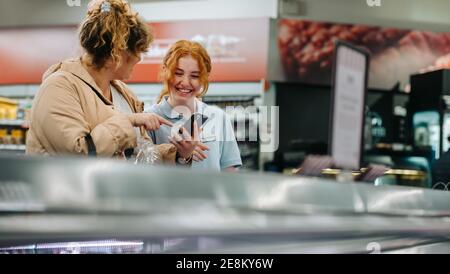 Buon dipendente del negozio di alimentari che aiuta la cliente femminile. Giovane dipendente che aiuta la cliente femminile al supermercato. Foto Stock