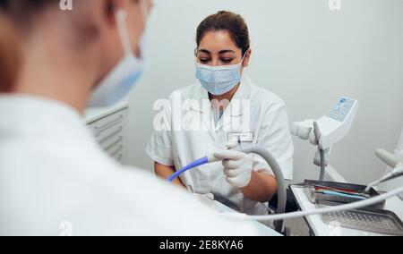 Infermiera femminile che assiste il medico in odontoiatria. Donna che indossa una maschera facciale che tiene un tubo mentre il medico fa un trattamento dentale su un paziente in clinica. Foto Stock