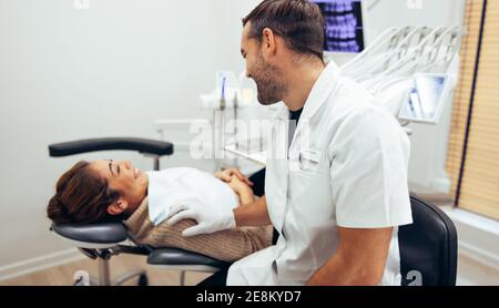 Dentista che parla con una paziente di sesso femminile seduto in sedia prima del trattamento. Paziente femminile e dentista sorridente in odontoiatria. Foto Stock