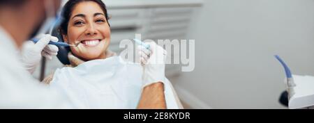 Dentista che esamina i denti di una paziente femminile in clinica dentale usando gli attrezzi dentali. Donna felice che ottiene il trattamento dentale. Foto Stock