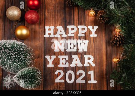 Cartolina di Natale, iscrizione con Capodanno 2021, sfondo marrone legno, decorazioni natalizie, ramo albero di Natale con coni e luci. Congratul Foto Stock