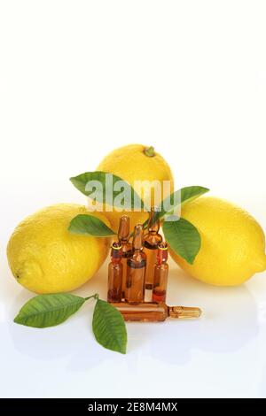 Iniezione di vitamina C. soluzione di vitamina C in ampolle di vetro, limoni su fondo bianco con riflessione. Ampolle e siero con vitamina C. Foto Stock