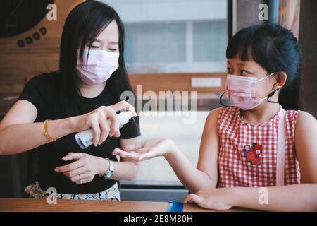 Madre e figlia asiatiche che indossano la maschera con alcool spray per Prevenire il Covid-19 Foto Stock