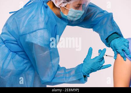 Una foto ingrandita di un operatore medico in attrezzature mediche di protezione, indossando una maschera monouso e uno scudo facciale, un vaccino sull'avambraccio del paziente Foto Stock