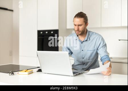Serio concentrato giovane analista di ragioniere maschile guardando lo schermo del portatile, facendo ricerca di mercato del commercio in linea, lavorando ad un progetto da casa Foto Stock