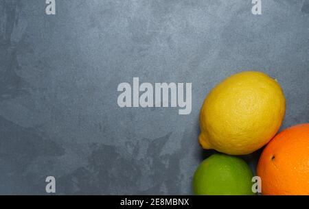 Arancio intero, lime e limone con pelle su fondo grigio stucco AGRUMI CITRICO Foto Stock