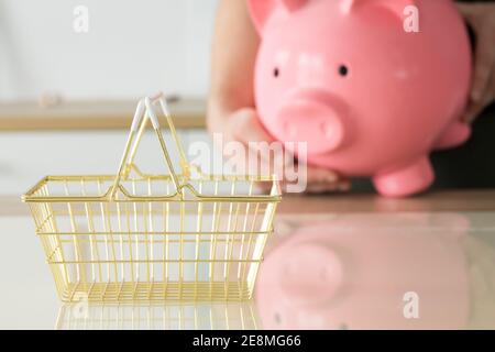 l'uomo ha una grande banca piggy nelle sue mani, un cestino di shopping dorato si trova sul tavolo davanti a loro. Il concetto di risparmio Foto Stock