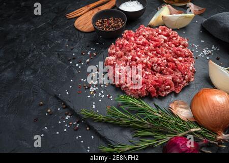 Carne sminuzzata fresca e succosa con spezie su un piatto piatto su fondo nero. Foto Stock