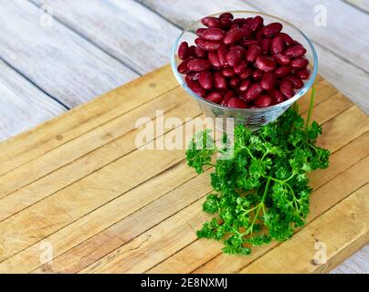 I fagioli rossi interi dell'alimento esposti in ciotola semplice di vetro per la vita sana dell'alimento con le erbe verdi fresche, il concetto, lo spazio della copia Foto Stock