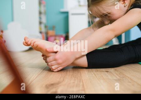 Primo piano le mani e i piedi della piccola ragazza ginnastica durante lo stretching allenamento a casa al piano di auto-isolamento periodo Foto Stock