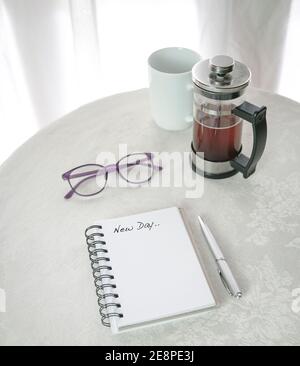 New Day, parole scritte su blocco note. Accanto alla pressa francese con caffè estratto. Su tavola bianca. Foto Stock