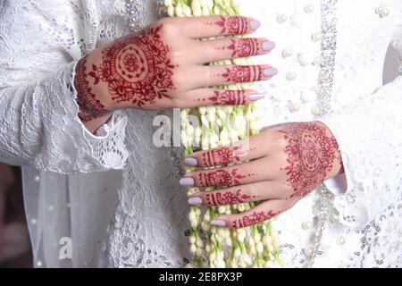 L'arte hennè sulla mano della sposa per la decorazione di nozze. Le mani che reggono i garlands di gelsomino. Il concetto di un matrimonio tradizionale giavanese, Indonesia Foto Stock